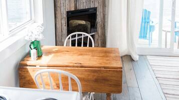 Een rustiek interieur met een houten tafel, witte stoelen, een aan een houten wand bevestigde televisie en een open haard.
