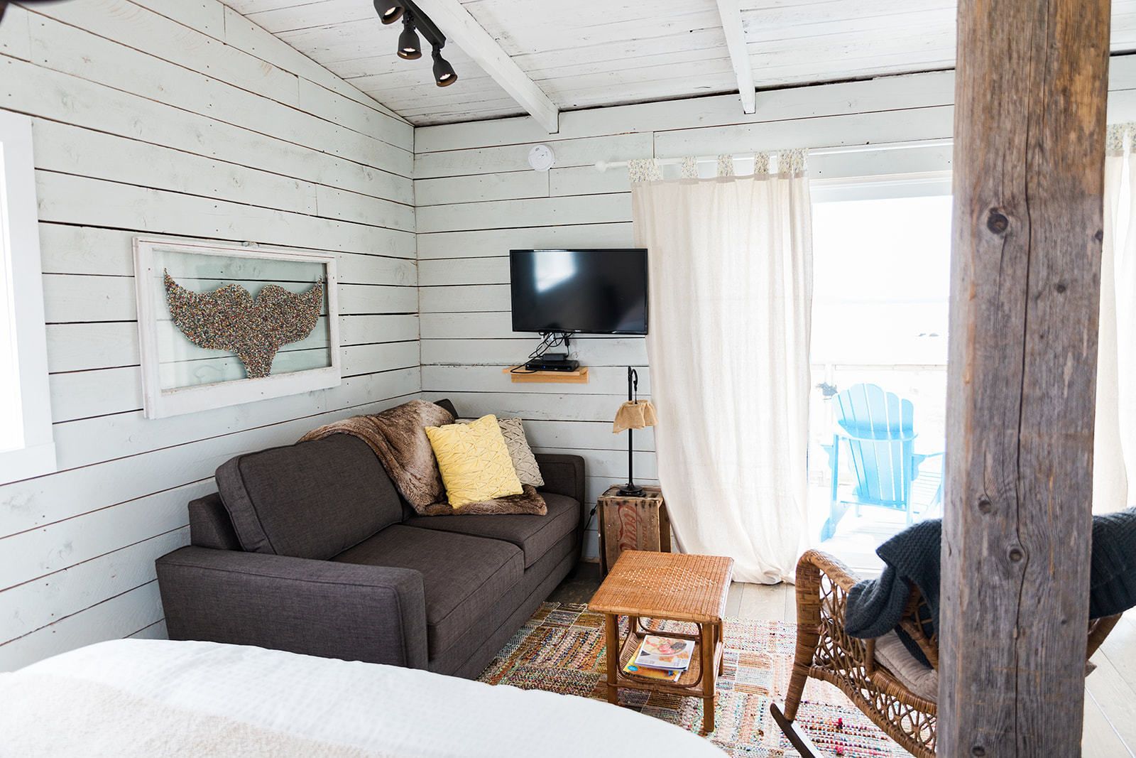 A cozy room with a grey sofa, a small table, a wicker chair, a television, and a decorative wall piece.
