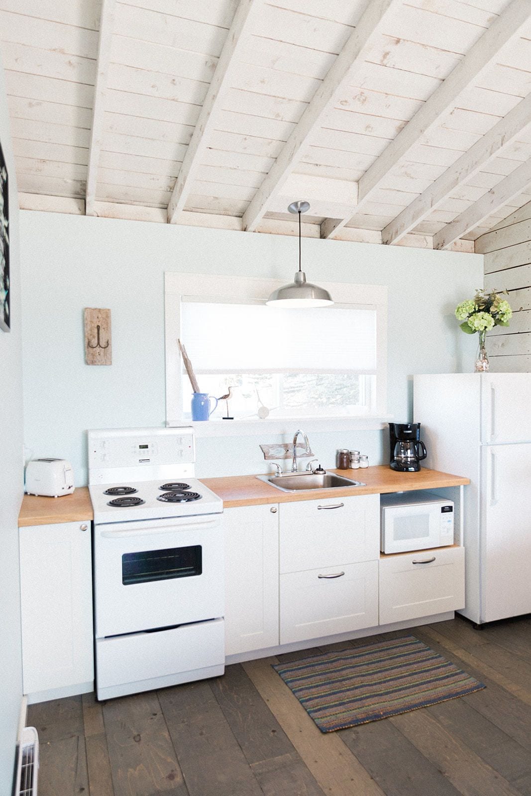 Une cuisine avec des armoires blanches, un plan de travail en bois, une cuisinière, un évier, une fenêtre et un luminaire suspendu.