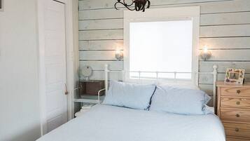 Un dormitorio con una cama, un aparador, una lámpara de araña y una ventana.