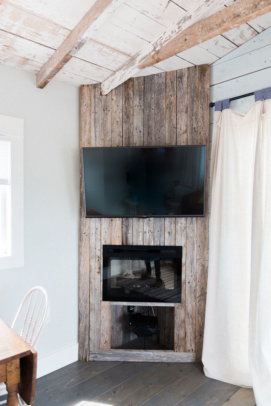 A room with a wooden wall, a flat-screen TV mounted above a fireplace, and a white curtain.