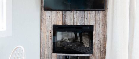 Habitació amb paret de fusta, televisió de pantalla plana penjada sobre una llar de foc, i cortina blanca.