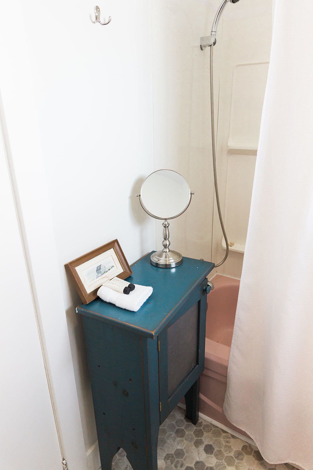 Un bagno con un piccolo mobile toilette, uno specchio rotondo, un quadro incorniciato e una tenda da doccia.