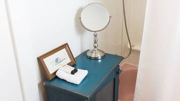 Un bagno con un piccolo mobile toilette, uno specchio rotondo, un quadro incorniciato e una tenda da doccia.
