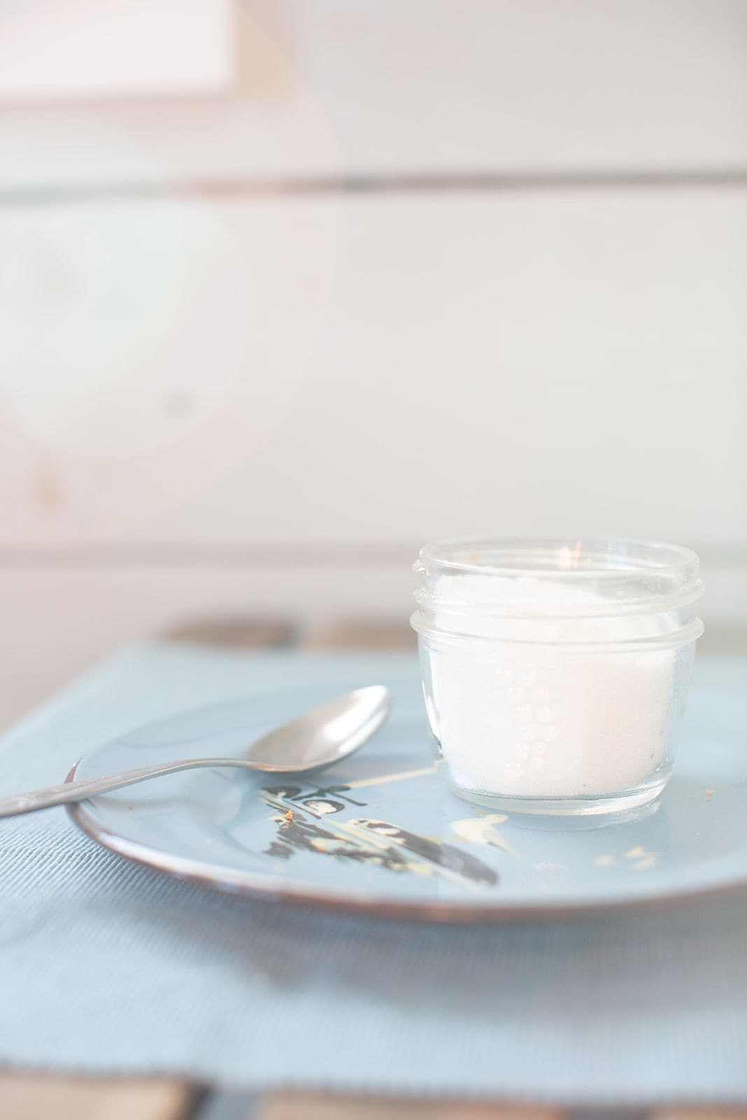 A small glass jar with a spoon on a blue plate.