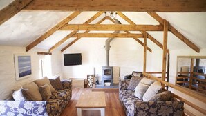 A cozy loft-style living room with wooden beams, a fireplace, and patterned sofas. - Merlin Farm Daymer and Treyarnon (Newquay)