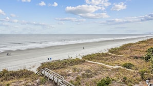 Een strand met een houten boardwalk naar de kust, zandstrand en een heldere lucht.