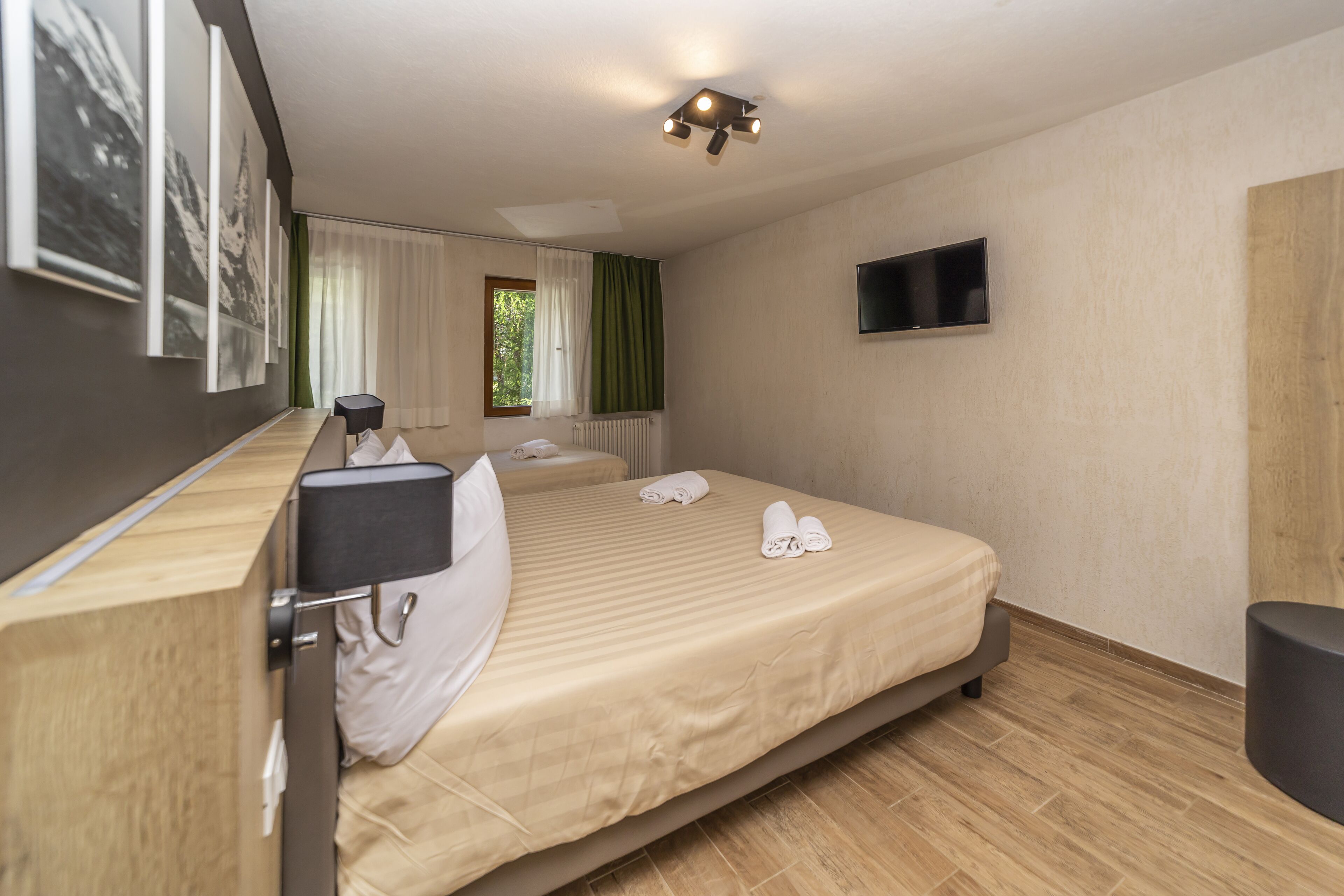 Une chambre d’hôtel avec un lit, un bureau, une chaise, une télévision et une fenêtre avec des rideaux.