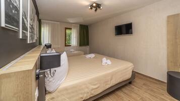 A hotel room with a bed, a desk, a chair, a TV, and a window with curtains.