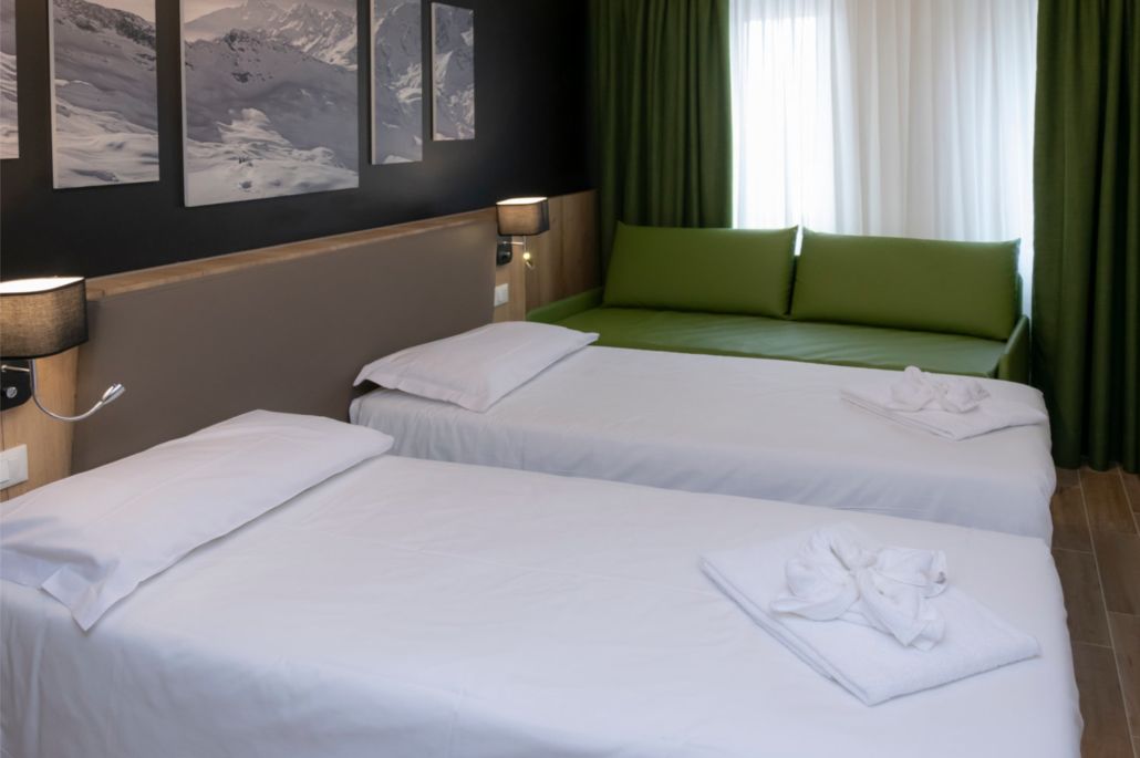 A hotel room with two beds, green curtains, and a mountain view.