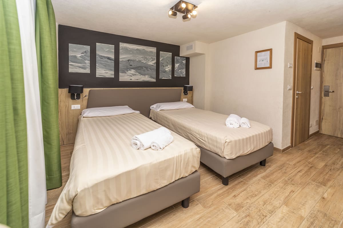 A hotel room with two beds, a wooden floor, and a wall with three framed pictures.