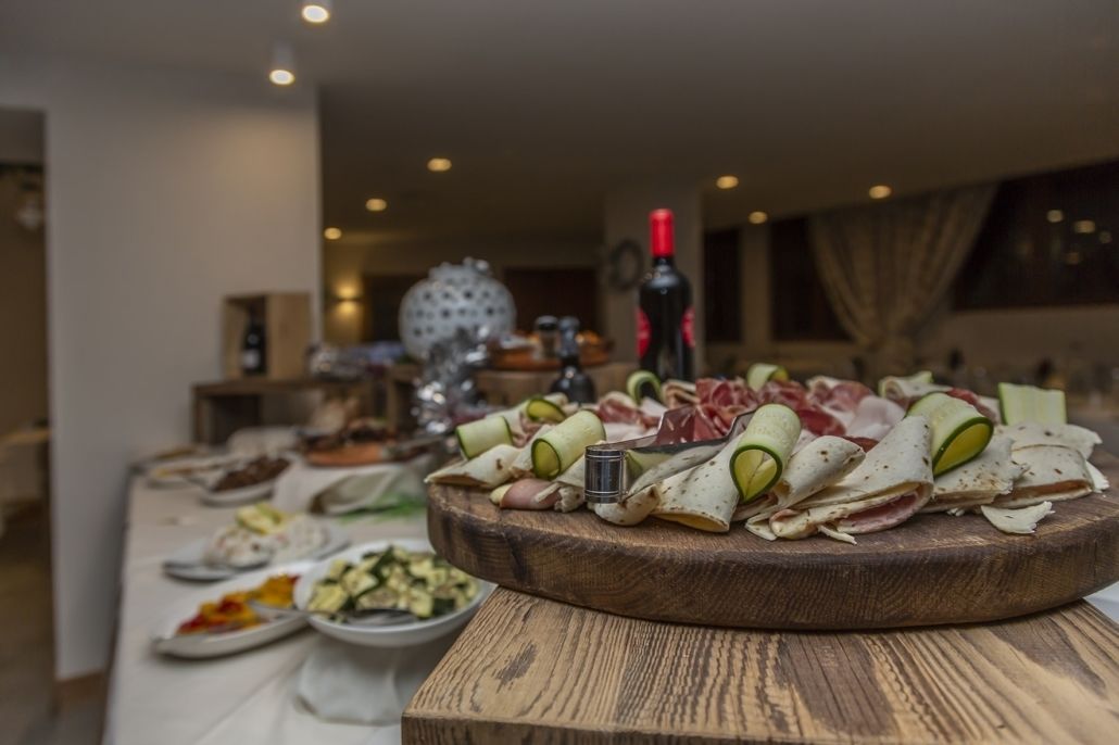 Una mesa de buffet con varios platos, incluyendo un recipiente central con carnes enrolladas y verduras, rodeado de otros alimentos.
