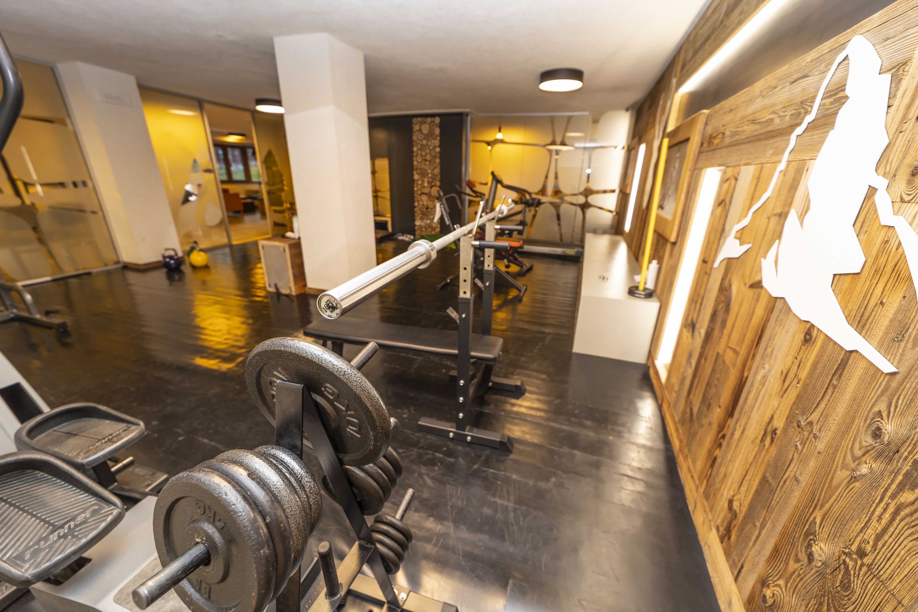 Une salle de sport équipée de matériel d’exercice, d’un miroir et d’un mur en bois orné d’une découpe en forme de silhouette.