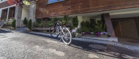 A modern two-story building with a wooden facade, a bicycle parked outside, and various potted plants and flowers in front.