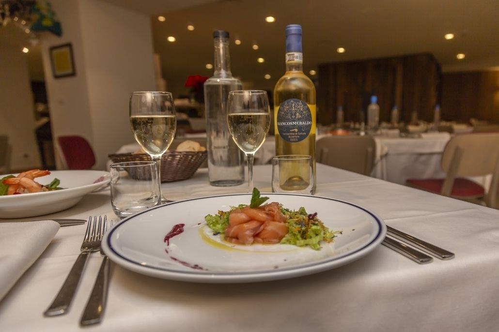 Una mesa de comedor con platos de comida, vasos y botellas de vino.