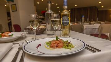 Una mesa de comedor con platos de comida, vasos y botellas de vino.
