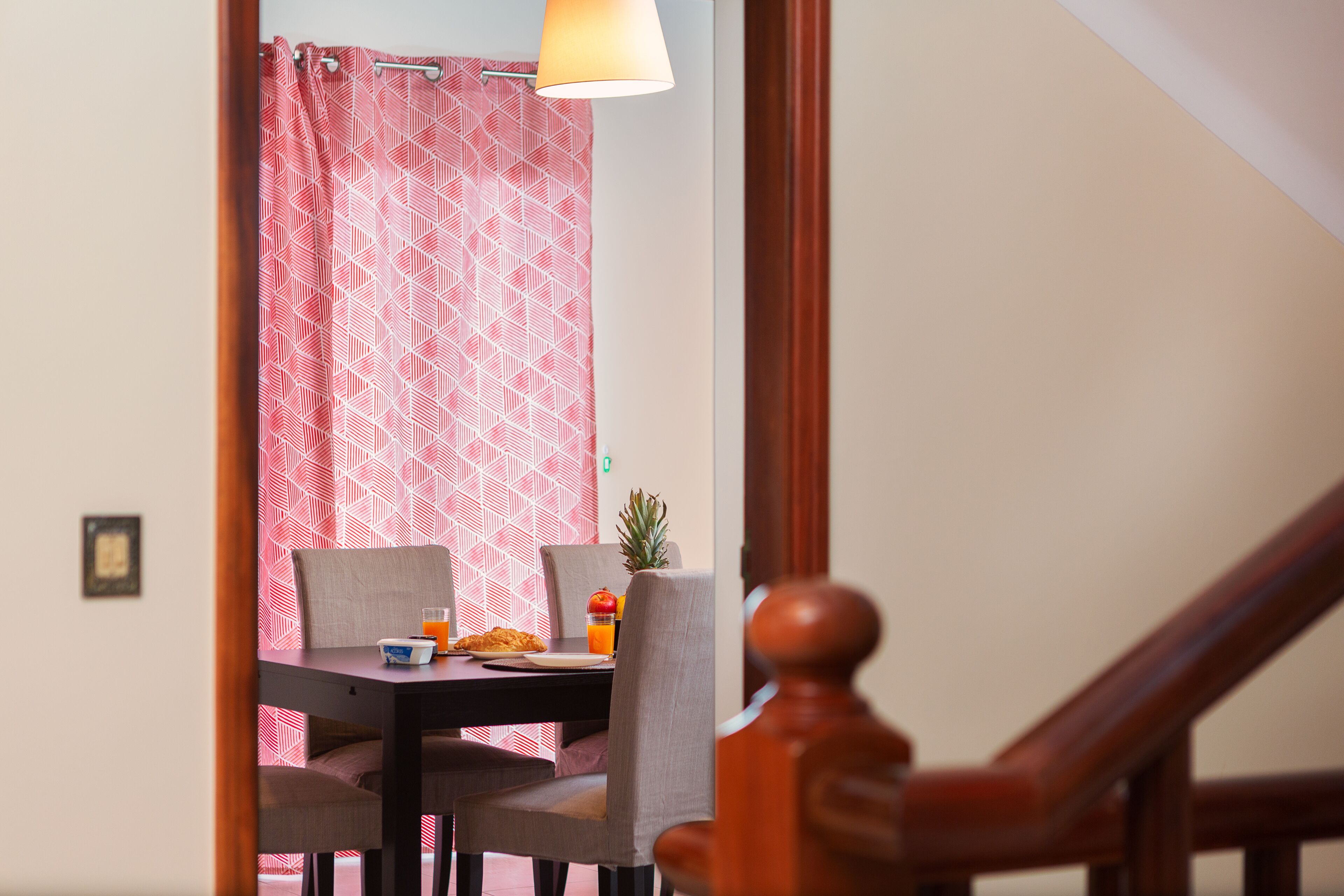 A dining area with a table set for two, chairs, a pineapple, and a glass of orange juice.