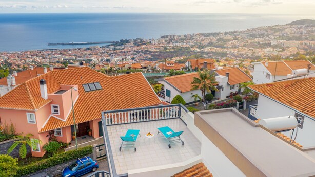 A residential area with terracotta-roofed houses, a balcony with two sun loungers, and a view of the sea and distant cityscape. - Villa Vista Mar - Holiday Home (Funchal)