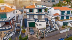 A multi-story residential building with a central staircase, balconies, and a car parked in the driveway. - Villa Vista Mar - Holiday Home (Funchal)