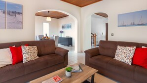 A living room with two brown sofas, a wooden coffee table, and a view of a dining area through an archway. - Villa Vista Mar - Holiday Home (Funchal)