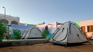 Twee tenten staan opgezet op zand, met gebouwen op de achtergrond.