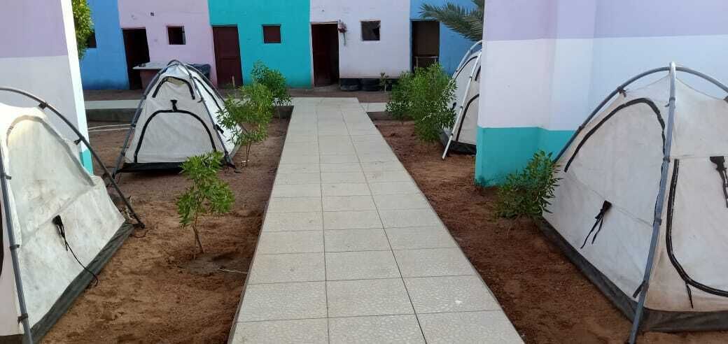 Un sendero que lleva a tiendas de campaña en un patio con edificios coloridos al fondo.