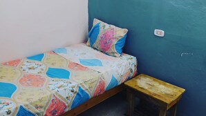 Een kleine eenpersoonskamer met een blauwgroene wand en een bloemenprint beddeken.