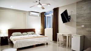 Habitación de hotel con cama, escritorio, silla, televisor y refrigerador.