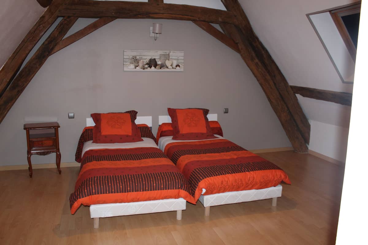 Une chambre avec deux lits, des poutres en bois, une petite table de chevet et un tableau au mur.