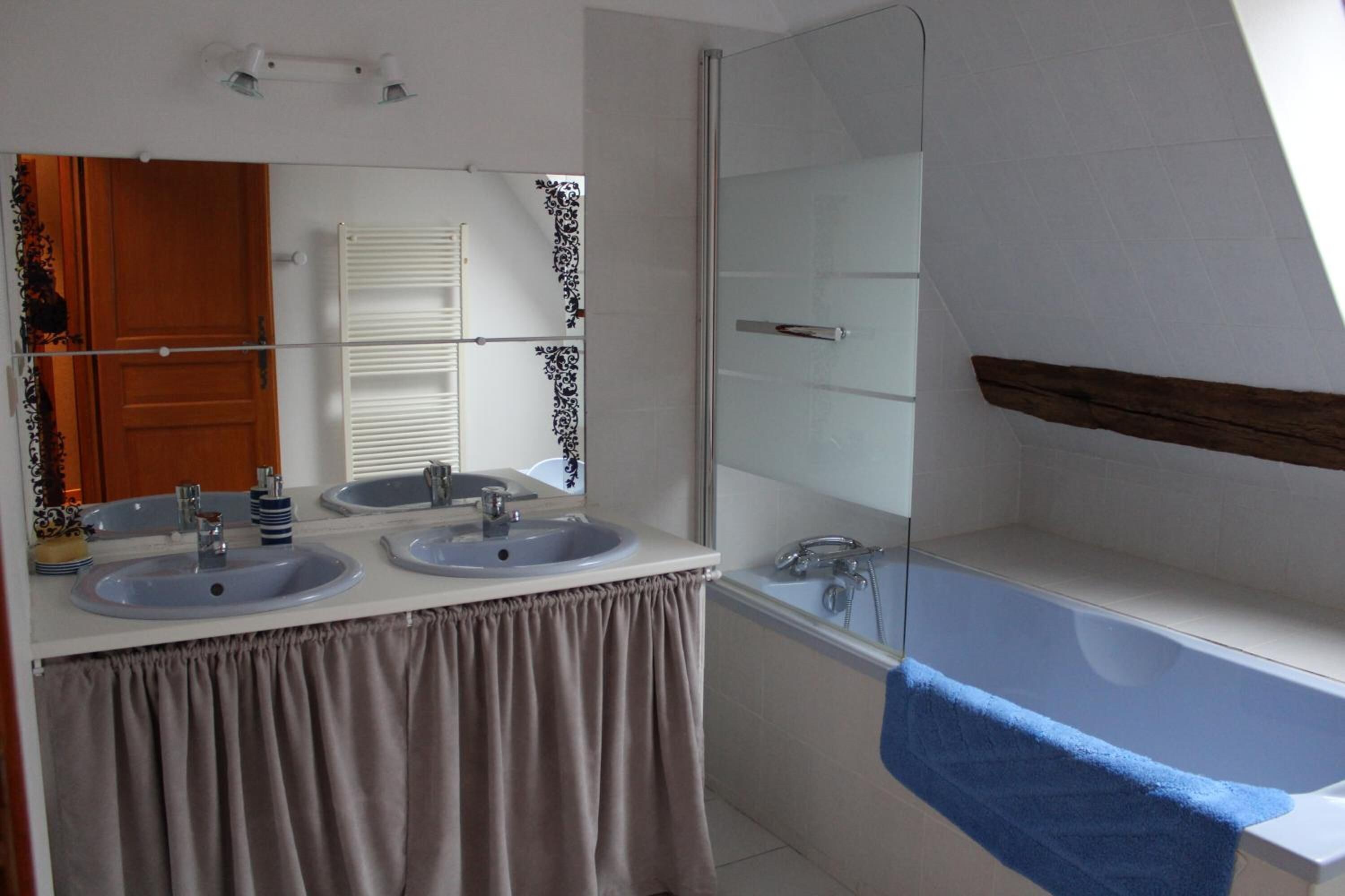A bathroom with two sinks, a glass shower enclosure, and a bathtub with a blue towel.