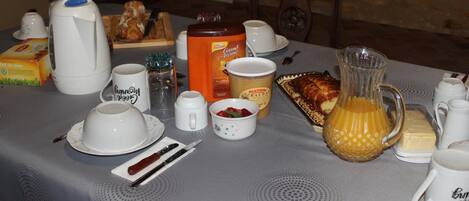 A breakfast table set with various items including a coffee maker, a jug, a croissant, and a bottle of Bauda.