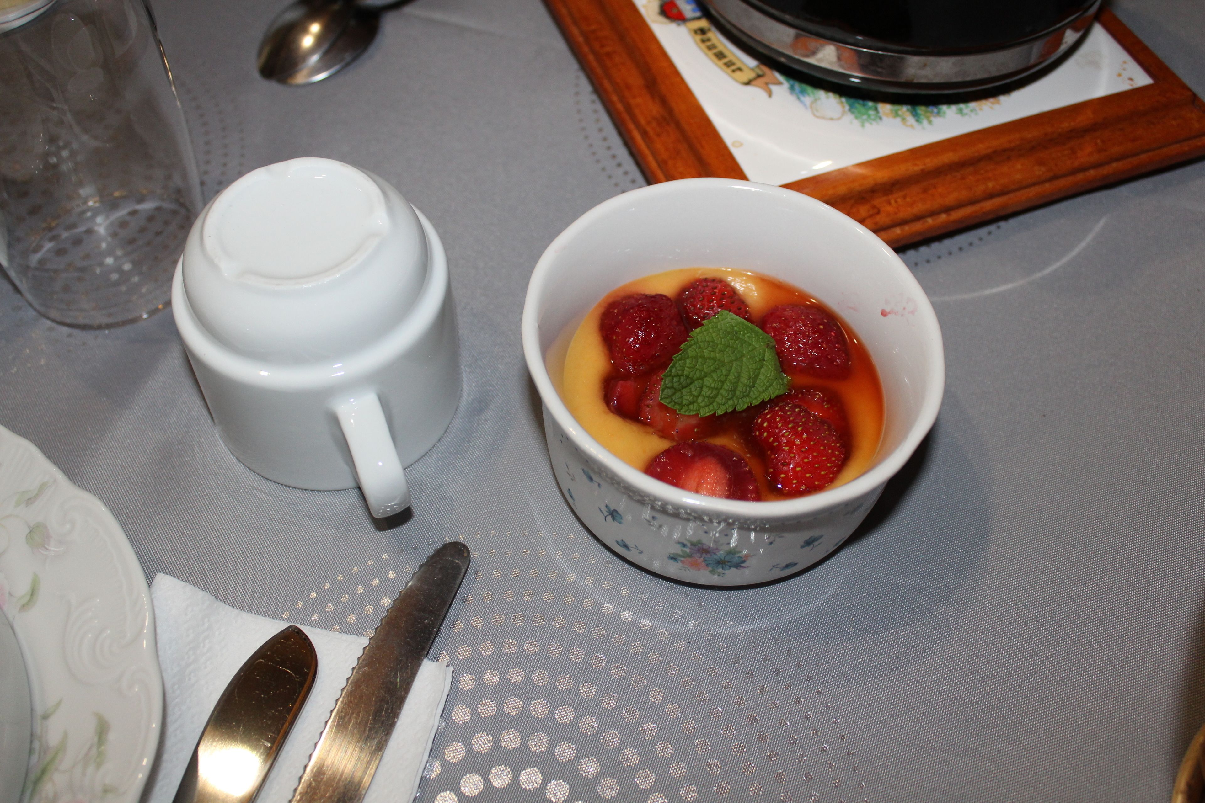 Une table avec une tasse en céramique blanche, un bol de fruits, une cuillère et un couteau.