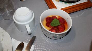 Une table avec une tasse en céramique blanche, un bol de fruits, une cuillère et un couteau.