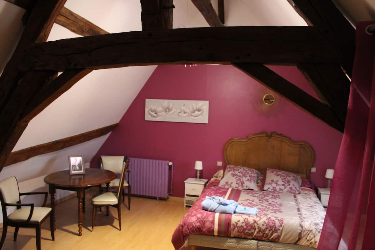 Une chambre avec un plafond en bois, un lit avec une literie à motifs floraux, une table de chevet, une chaise et un radiateur.