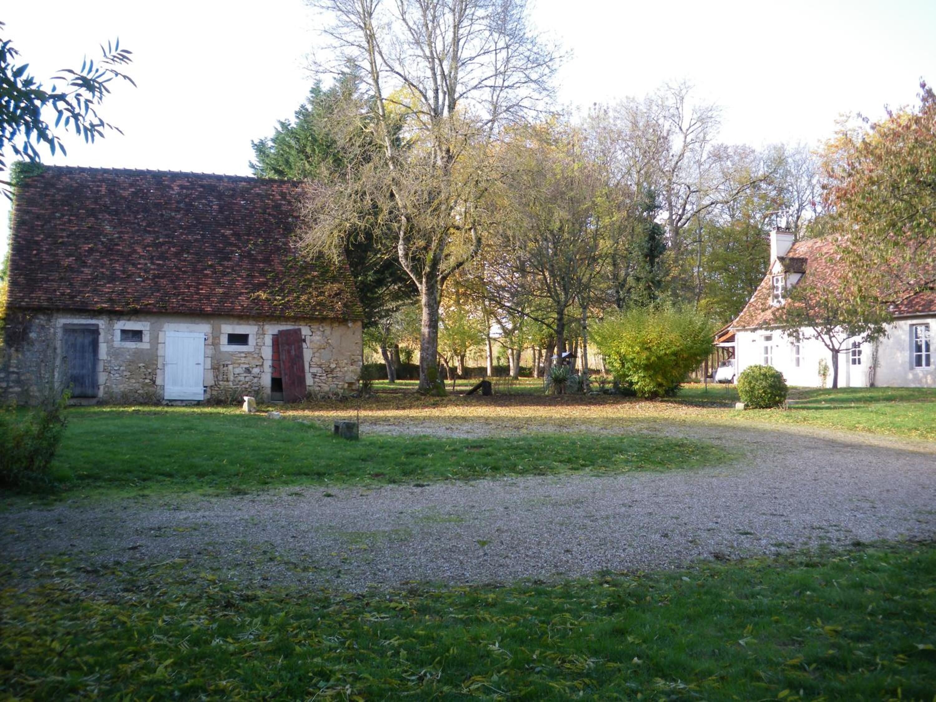 A rural property with a stone building, a gravel driveway, and surrounding trees.