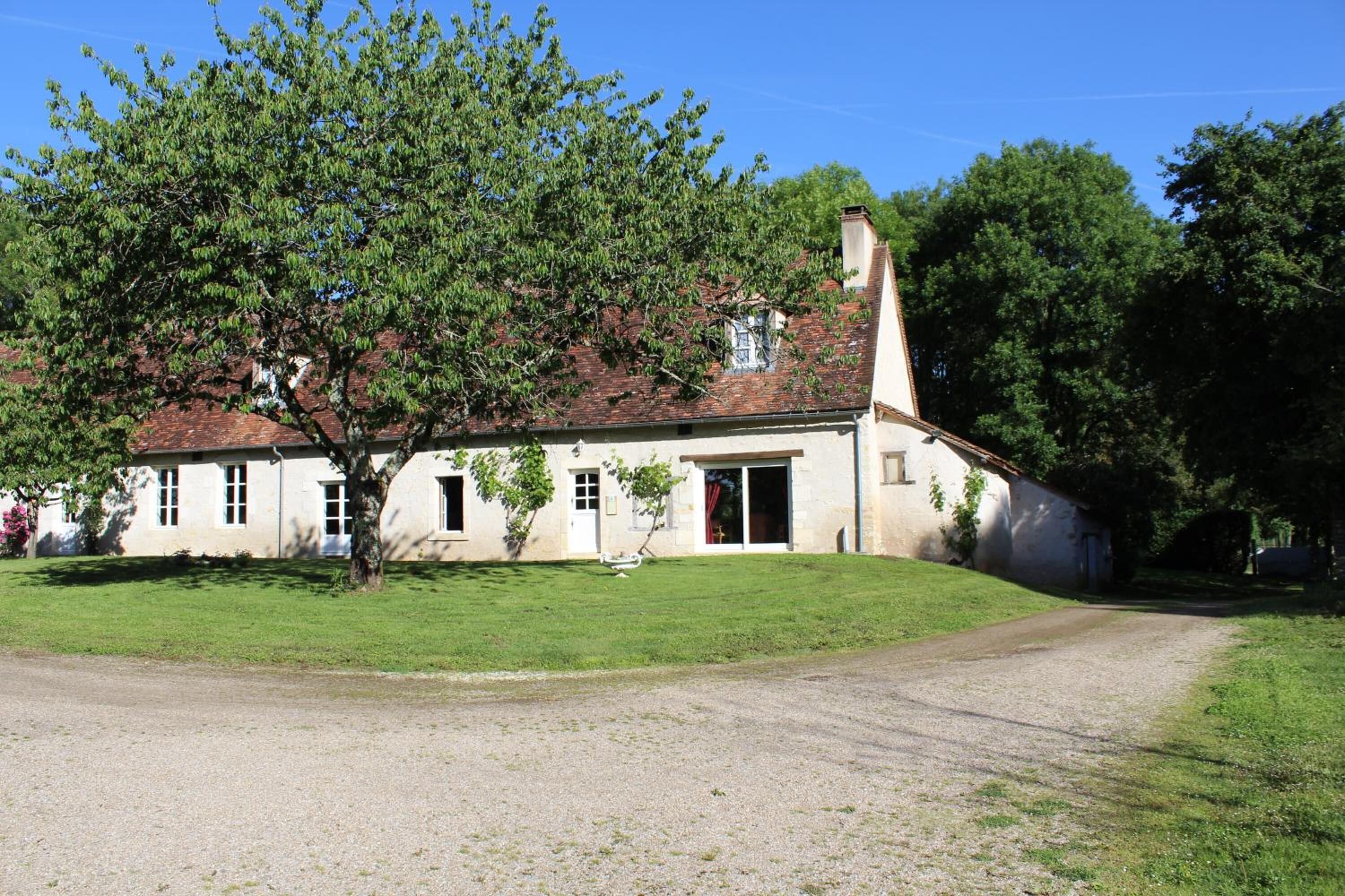 A two-story building with a red-tiled roof, a large tree in front, and a gravel driveway.