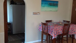 A dining area with a table set for four, wooden chairs, and a painting of a pier on the wall.