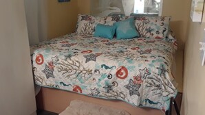A bed with a patterned bedspread featuring sea creatures and a window with curtains.