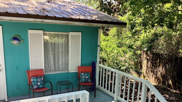 A turquoise building with a white porch and two chairs with starfish cushions.