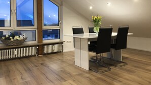Un coin repas comprenant une table, des chaises, un vase avec des fleurs et une fenêtre donnant sur le ciel.