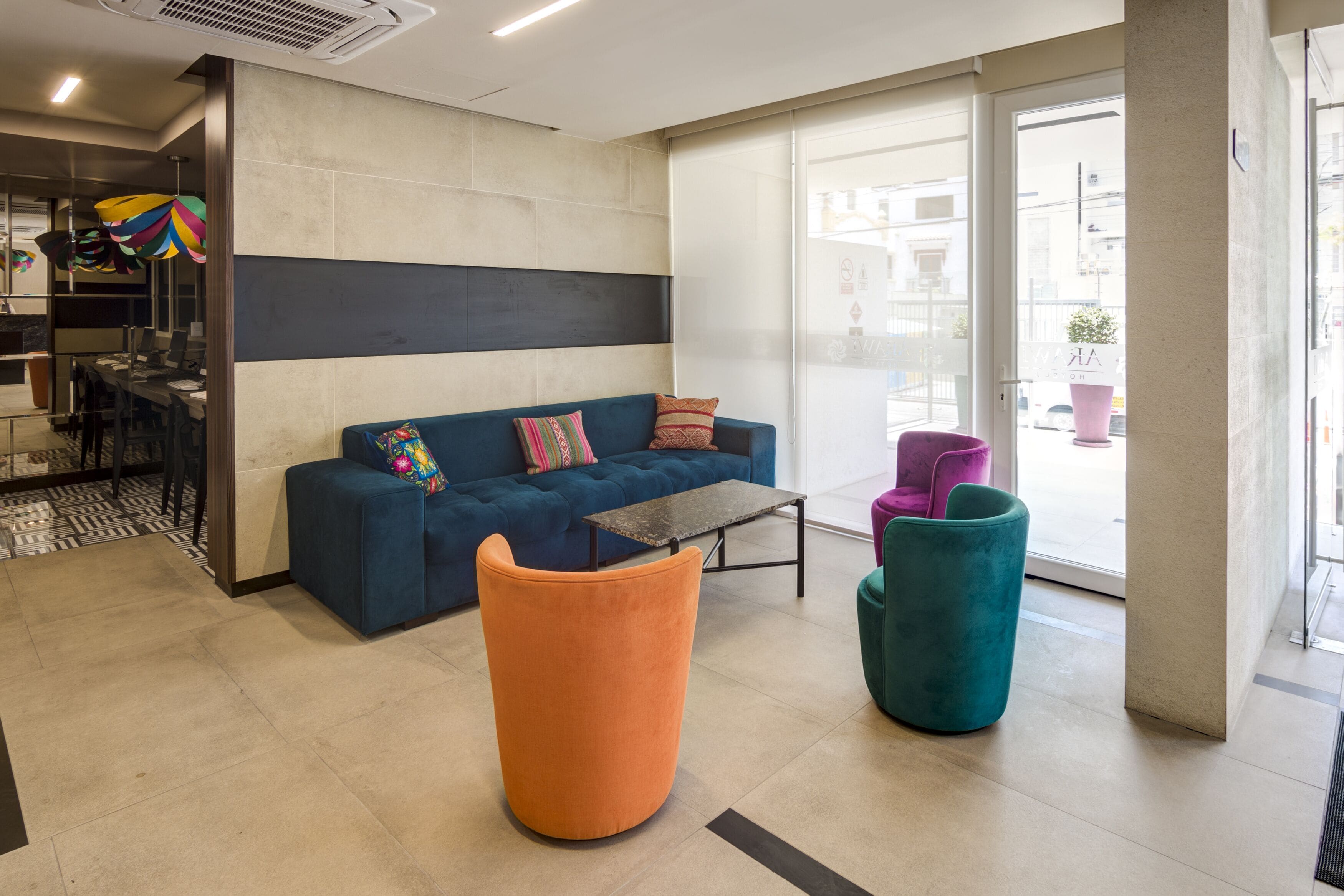 A modern lobby with a blue sofa, orange ottoman, teal chair, and a small table.