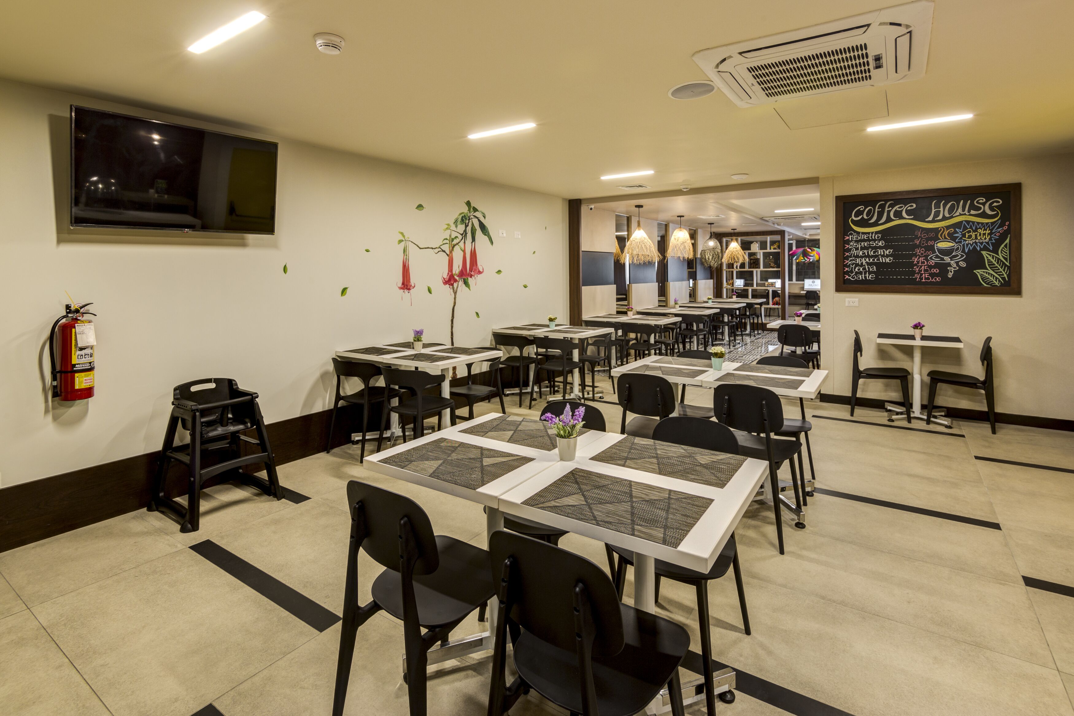 Un restaurante limpio y bien iluminado con varias mesas y sillas, un extintor y un menú en una pizarra en la pared.