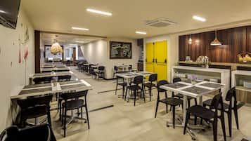A modern cafe with multiple tables and chairs, a yellow door, and a chalkboard menu.