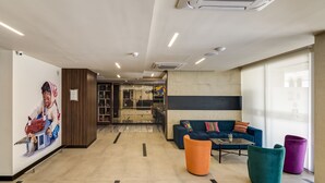 A modern lobby with a blue sofa, orange and teal ottomans, and a mural on the wall. - Arawi Miraflores Express (Lima)