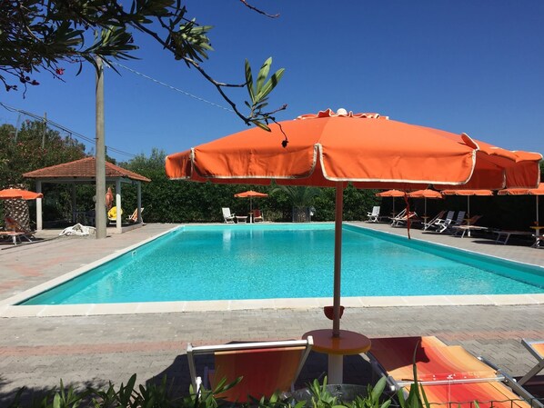 Piscina com espreguiçadeiras e guarda-sóis laranja.