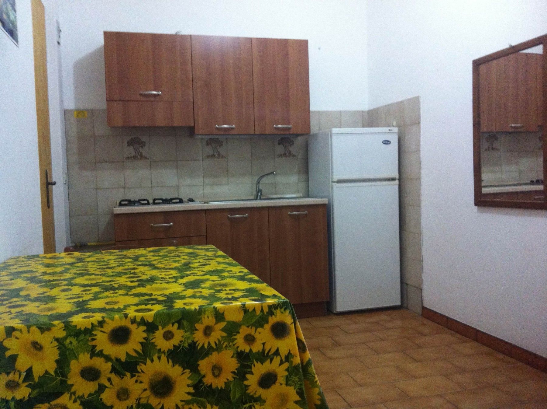 A small kitchen with wooden cabinets, a white refrigerator, and a tiled backsplash.