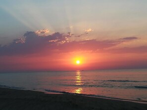 Um pôr do sol sobre uma praia, com o sol refletindo na água.
