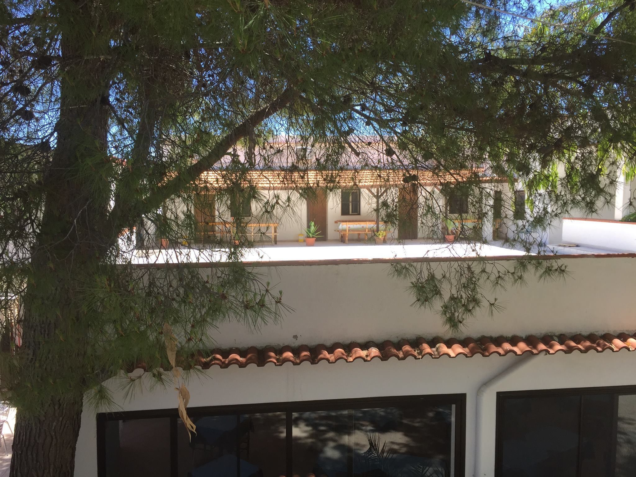 Un edificio con techo de tejas, un balcón con mesa y sillas, y un ventanal grande.