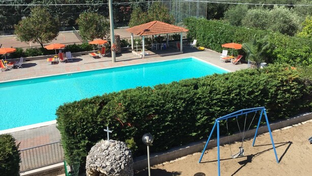A swimming pool with lounge chairs and umbrellas, surrounded by greenery and a gazebo.