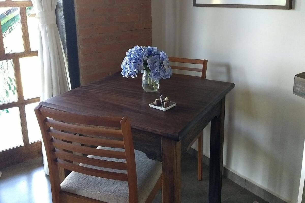 A dining table with two chairs, a vase with flowers, and a framed picture on the wall.